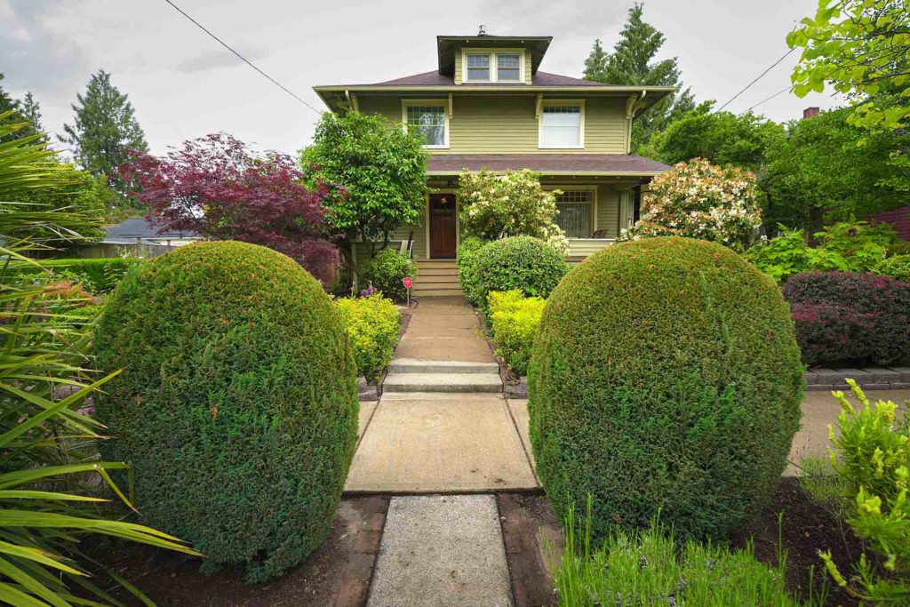 Green century-old house with beautifully manicured landscaping in front