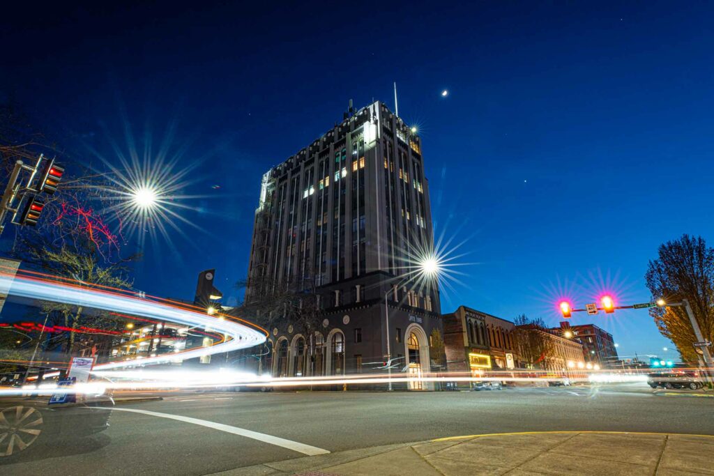 The Capitol Tower in downtown Salem at night with streaking lights on the road.